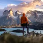 A hiker stands at sunrise in Torres del Paine, Chile, overlooking majestic mountains and a tranquil lake.